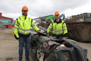 Her står to ansatte i HRS Metallco og holder hendene på en bil som har blitt presset av en av våre maskiner.